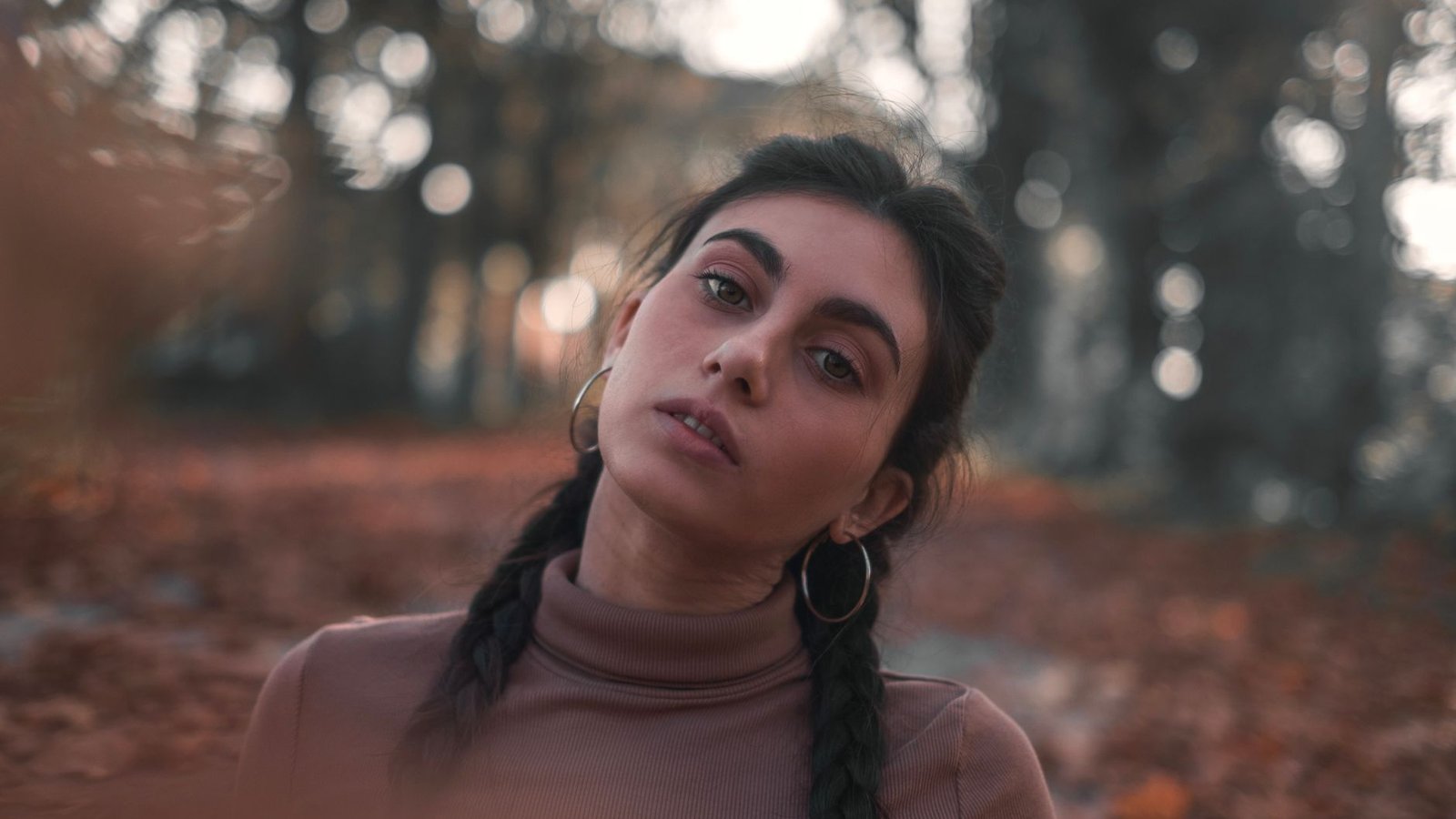Close-up portrait of a woman in a turtleneck amidst autumn leaves with a blurred background.