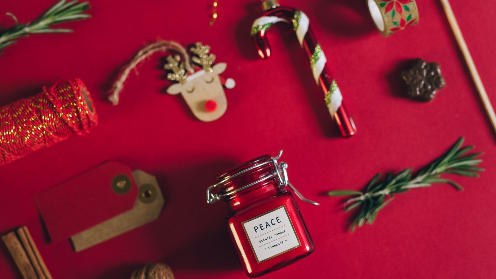 Top view of Christmas decorations and scented candle on a red surface.