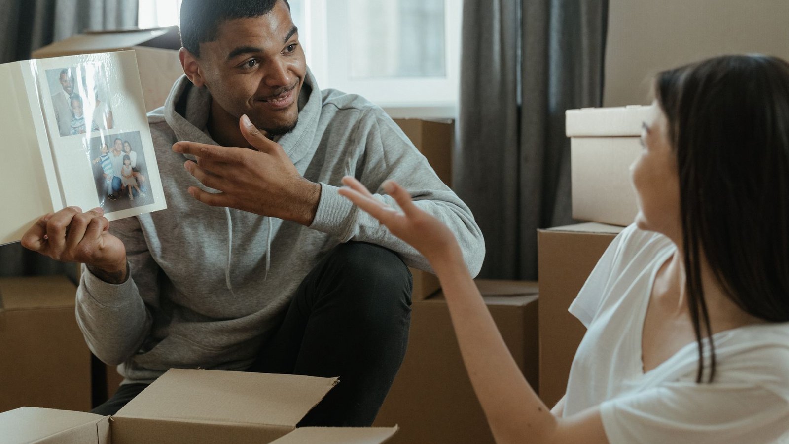 A couple shares memories from a photo album while unpacking boxes in their new home.
