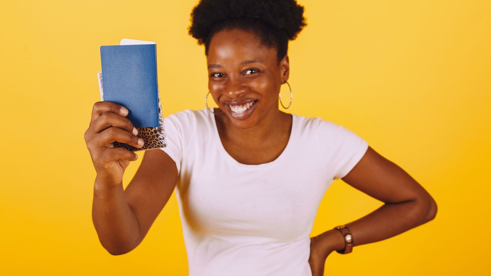 Smiling woman holding a passport, ready for a travel adventure against a yellow background.