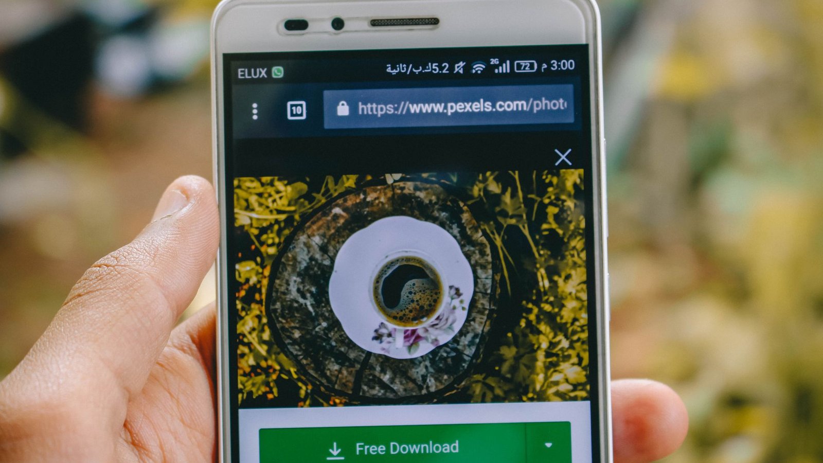 Close-up of a smartphone showing a coffee cup image on a screen outdoors.